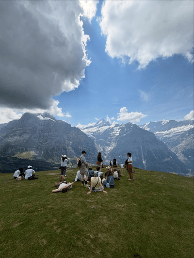 People sitting on a grassy ridge above the Grindelwald mountains and glacier