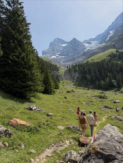 Hikers walking a green alpine valley trail toward the mountains