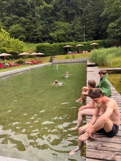 Guests beside a natural swimming pond surrounded by forest